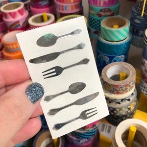 May include: A sheet of silver sticker decals featuring a set of six kitchen utensils: two spoons, two forks, and two knives.
