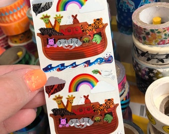 May include: A sheet of colorful stickers featuring a rainbow, clouds, and a Noah's Ark with animals. The ark is filled with a variety of animals, including giraffes, elephants, lions, and a hippopotamus. The stickers are perfect for adding a touch of whimsy to any project.