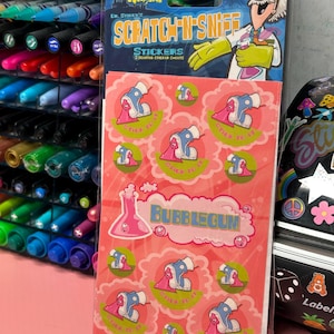 May include: A pink and green package of Dr. Stinky's Scratch 'n Sniff Stickers. The package features a cartoon scientist and a beaker with the text "Bubblegum". The stickers are of a pink cartoon foot with blue shoes and the text "Stick to it".