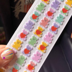 May include: A sheet of colorful fuzzy teddy bear stickers with red hearts. The bears are in various colors including yellow, green, pink, purple, and light blue.