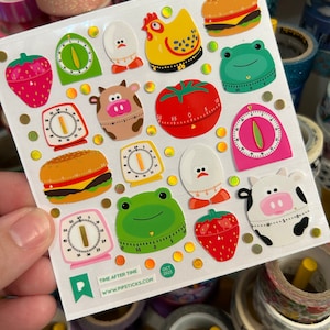 May include: A sheet of colorful stickers featuring various kitchen timer designs. The stickers include a cow, a chicken, a tomato, a strawberry, a hamburger, a frog, and an egg. The stickers are printed with the text "TIME AFTER TIME" and "WWW.PIPSTICKS.COM".