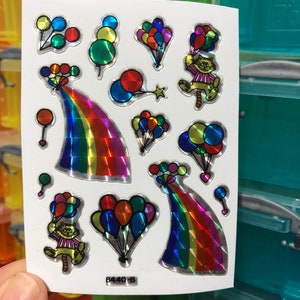 May include: A sheet of colorful holographic stickers featuring a rainbow, a cat holding balloons, and various balloons in different colors. The stickers are on a white background and have a shiny, iridescent finish. The text "8440-B" is printed in the bottom right corner.