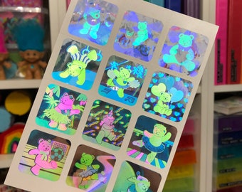 May include: A sheet of holographic stickers featuring a variety of colorful bears in different poses. The bears are wearing hats, holding balloons, and performing various activities. The stickers are perfect for adding a touch of whimsy to any project.