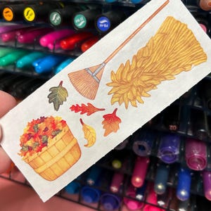 May include: A sheet of fall-themed stickers with a brown broom, a basket of colorful leaves, and various leaf shapes in shades of red, orange, and yellow.
