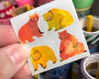 May include: A sheet of colorful bear stickers with a holographic finish. The bears are in various shades of orange and yellow.