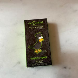 Puede incluir: Un delineador de ojos en gel The Simpsons Treehouse of Horror negro y verde con una imagen de dibujos animados de un cuervo y el texto "Matt Groening".