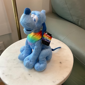 May include: A blue plush dog toy with a rainbow collar. The toy has a black tag that reads "Rainbow Disney Collection". The dog is sitting on a white marble table.