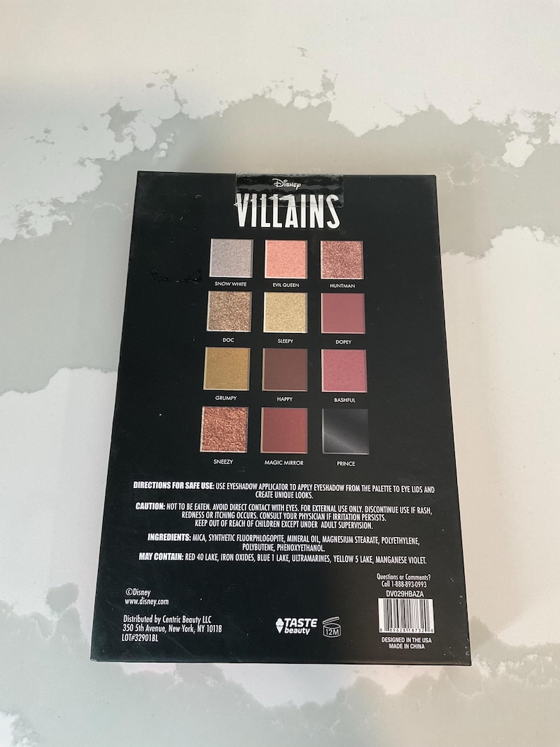 May include: A black eyeshadow palette featuring the word "VILLAINS" and Disney branding. The palette contains twelve eyeshadow shades with names like "Snow White," "Evil Queen," and "Prince." The back of the palette includes safety instructions and ingredient information.