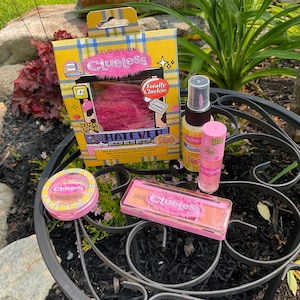 Peut inclure: Une collection de produits de maquillage Revolution x Clueless, comprenant une palette de fards à paupières, une huile à lèvres et un spray fixateur. L'emballage présente un motif à carreaux jaunes avec des accents roses et le texte "Clueless."