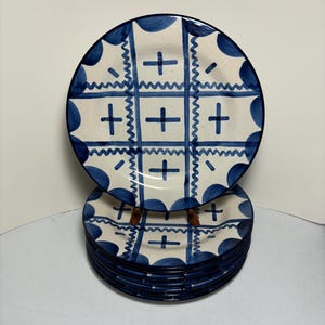 May include: A stack of eight blue and white ceramic dinner plates with a geometric pattern. The plates have a scalloped edge and a blue rim.