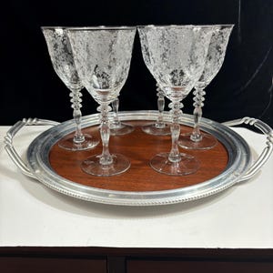 May include: Set of six clear glass wine glasses with a frosted etched design, displayed on a silver tray with a wooden base.