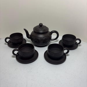 May include: A dark brown tea set featuring a teapot with a lid and four teacups with saucers. The teapot and cups have embossed designs. The set is made of ceramic and is suitable for serving tea.