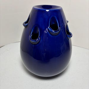 May include: A cobalt blue ceramic vase with a bulbous body and a flared top. The vase features several oval openings around the sides. The glossy finish enhances the rich color, making it a decorative accent piece.