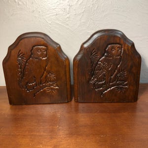 May include: A pair of wooden bookends featuring carved owls. The bookends are dark brown and have a rustic look.