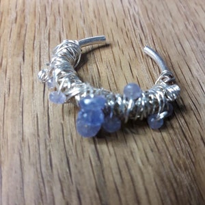 May include: A silver wire wrapped hoop earring with light blue gemstone accents.