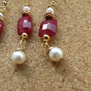 Può includere: Un paio di orecchini con dettagli in pietra preziosa rossa e perla. Gli orecchini sono realizzati con filo d'oro e presentano un ciondolo in pietra preziosa rossa e una perla bianca.