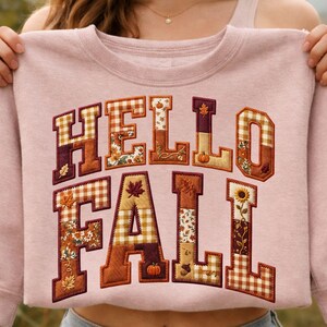 Peut inclure: Un sweat-shirt &agrave; col rond rose clair avec l'inscription HELLO FALL en grandes lettres majuscules. Chaque lettre est remplie d'un motif patchwork sur le th&egrave;me de l'automne, incluant du vichy orange, des tournesols, des citrouilles et des feuilles.