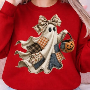 Op de afbeelding: Een felrood sweatshirt met lange mouwen en een centrale afbeelding van een cr&egrave;mekleurige geest met een strik met patroon. De geest is voorzien van diverse stoffen patches in ruit- en bloemenprints en houdt een klein pompoenemmertje vast.