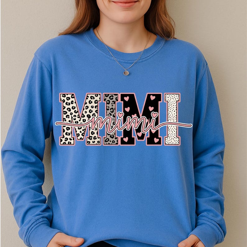 May include: A blue long-sleeve sweatshirt featuring the word "MIMI" in a decorative design. The letters have a leopard print, black with pink hearts, and white polka dot pattern. The word "Mimi" is in a cursive font.