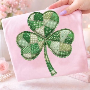 Może przedstawiać: Zielona aplikacja w kształcie koniczyny z patchworkowym wzorem, przedstawiająca różne wzory i odcienie zieleni. Koniczyna jest wyświetlana na różowej powierzchni, prawdopodobnie tkaninie, z ręką, która ją trzyma. Projekt jest prawdopodobnie na Dzień Świętego Patryka.