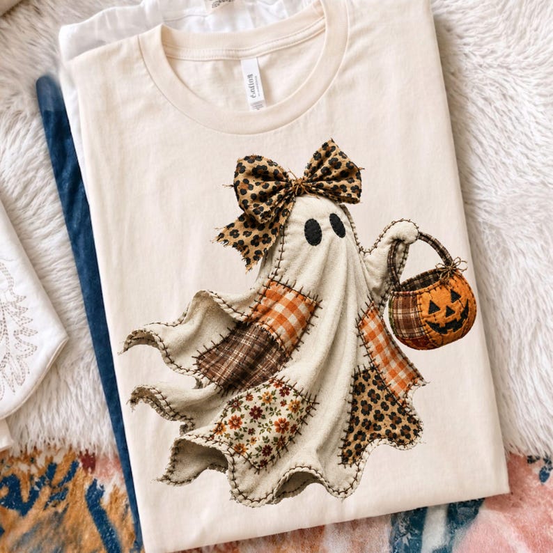 Pu&ograve; includere: Una t-shirt a maniche corte color crema con la grafica di un fantasma composto da vari ritagli di tessuto, inclusi motivi a quadri, floreali e leopardati. Il fantasma indossa un fiocco leopardato e tiene in mano un secchiello a zucca arancione.