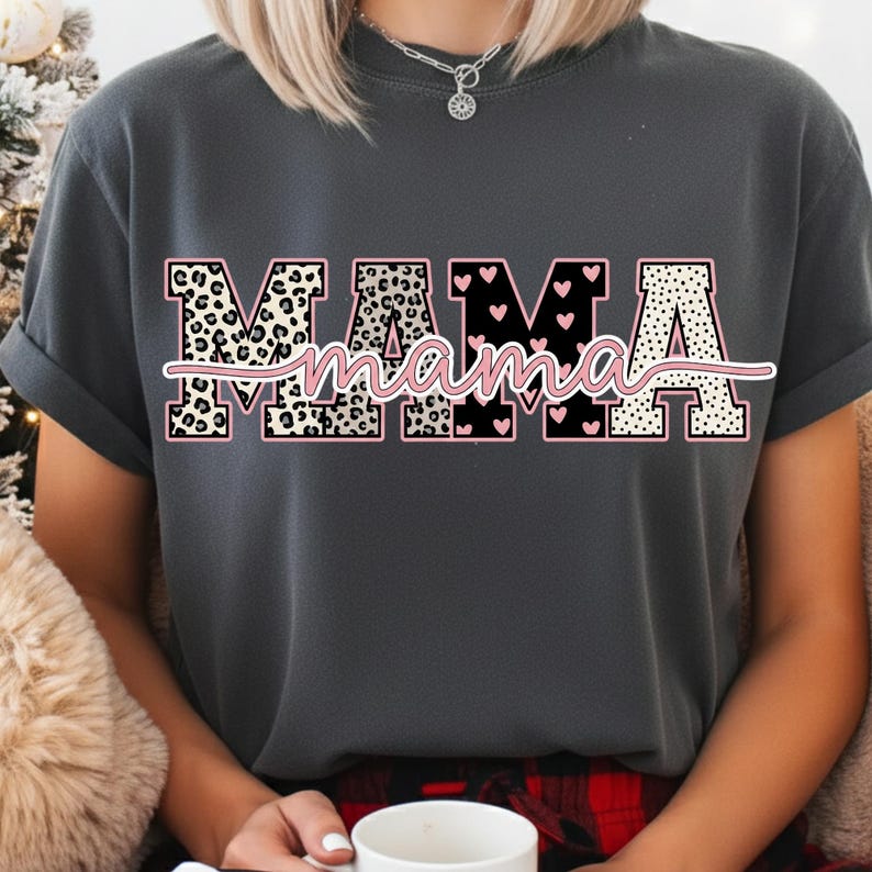 May include: Dark gray t-shirt with the word "MAMA" in a decorative design. The letters have leopard print, black with pink hearts, and white polka dots. The word "mama" is written in cursive in pink.