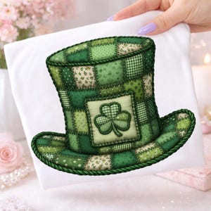 Puede incluir: Un sombrero de duende verde de patchwork con un emblema de trébol. El sombrero presenta varios tonos de cuadrados de tela verde, cosidos con un ribete de cuerda verde oscuro. El trébol está centrado en la parte delantera del sombrero, añadiendo un toque festivo. El sombrero se muestra sobre una superficie blanca.