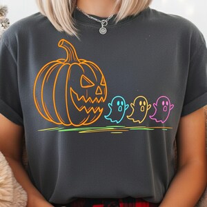 Op de afbeelding: Donkergrijs T-shirt met een neon oranje pompoen en drie kleurrijke geesten. De geesten zijn omlijnd in blauw, geel en roze. Het ontwerp is gedrukt op een zacht, comfortabel T-shirt.