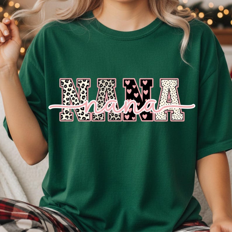 May include: A dark green t-shirt with the word "NANA" in a decorative font. The letters have a pink outline and are filled with leopard print, hearts, and polka dots. A cursive "nana" is written underneath.