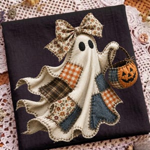 Op de afbeelding: Een stoffen spookornament met een cr&egrave;mekleurig lichaam voorzien van diverse lapjes in oranje ruitjes, bruine tartan, blauwe denim en bloemenpatronen. Het spook heeft twee zwarte ogen, een grote bloemstrik bovenop en draagt een pompoenmandje.