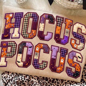 May include: A beige fabric surface featuring the text HOCUS POCUS in large, appliqued letters. Each letter is constructed from various fabric patches in orange, purple, and black, displaying patterns of ghosts, bats, spiders, and webs.