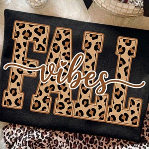 May include: Black t-shirt with the words "FALL vibes" in a brown and leopard print design. The word "FALL" is in large block letters, and "vibes" is in a cursive font.