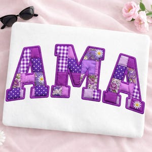 May include: A white sweatshirt featuring the letters AMA in a large, block-style font. The letters are filled with a patchwork design of purple, lavender, and white fabrics, including gingham, polka dot, and floral patterns with daisy motifs.