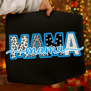 Puede incluir: Bolso tote negro con la palabra "MAMA" en letras grandes y audaces. Las letras tienen un contorno azul y están rellenas de varios patrones, incluyendo estampado de leopardo, cruces y lunares. La palabra "mama" está escrita en cursiva debajo.