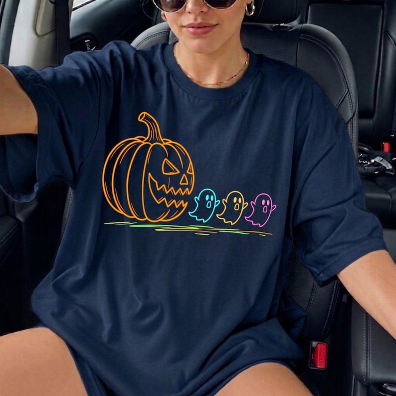 Op de afbeelding: Marineblauwe t-shirt met een Halloween-ontwerp. De afbeelding toont een oranje pompoen en drie kleurrijke geesten. De neon contouren cre&euml;ren een feestelijke en opvallende uitstraling.