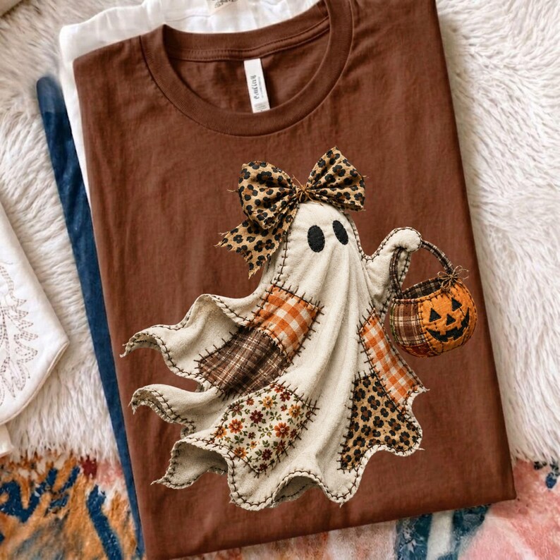 Pu&ograve; includere: Una t-shirt marrone a girocollo con la grafica di un fantasma composto da vari tessuti a motivi, tra cui tartan, fiori e stampa leopardata. Il fantasma indossa un grande fiocco leopardato e tiene in mano un piccolo secchiello a forma di zucca.