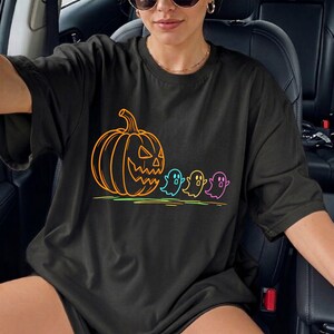 Op de afbeelding: Zwart T-shirt met een neon oranje pompoen en drie kleurrijke geesten. Het ontwerp heeft een Halloween-thema, met de pompoen en geesten omlijnd in heldere kleuren. Het shirt is een casual, oversized stijl.