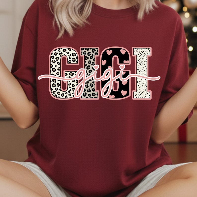May include: A maroon sweatshirt featuring the word "GIGI" in a bold, multi-textured design. The letters incorporate leopard print, black with pink hearts, and a dotted pattern. The word "gigi" is written in a cursive font across the letters.