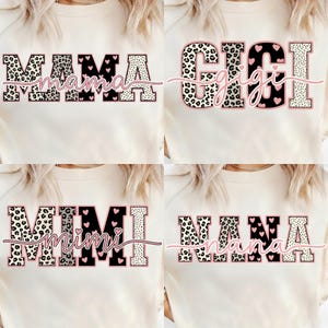 May include: Four cream-colored sweatshirts with the words "MAMA", "GIGI", "MIMI", and "NANA" printed on them. The text is in a mix of leopard print, black, and white, with pink heart accents. The sweatshirts are casual wear.