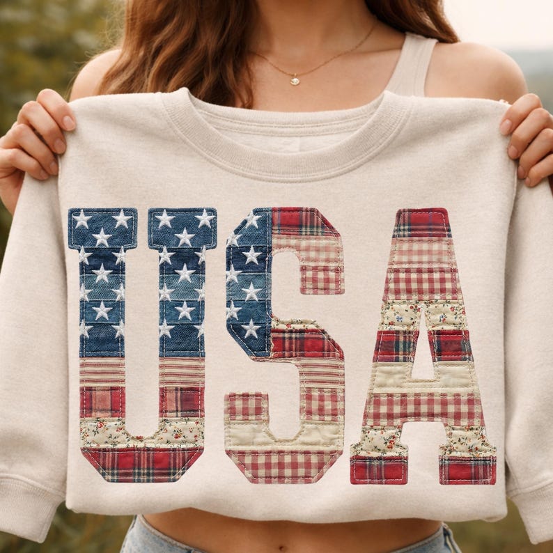 May include: Cream-coloured sweatshirt featuring the word "USA" in a patchwork design. The letters are decorated with denim, stars, and red plaid patterns, creating a patriotic theme.