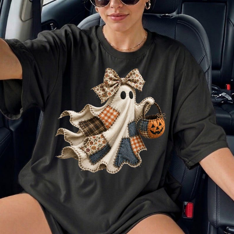 Op de afbeelding: Een zwart T-shirt met korte mouwen en een afbeelding van een geest gemaakt van verschillende stoffen lapjes. De geest draagt een grote strik met patroon op het hoofd en draagt een klein oranje pompoenemmertje. Het ontwerp bevat ruitjes en bloemmotieven.