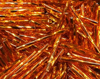May include: A close-up of a pile of orange glass rods. The rods are all the same size and shape, and they are arranged in a random pattern. The rods are shiny and reflect the light.