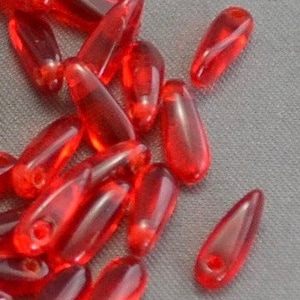 May include: A collection of translucent red teardrop-shaped beads. Each bead has a small hole at the top for stringing. The beads are scattered on a gray surface, showcasing their glossy texture and vibrant color.
