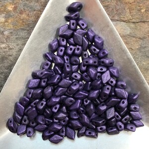 May include: A pile of small, dark purple, faceted glass beads with two holes in each bead.