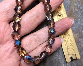 May include: A strand of iridescent glass beads in shades of brown, pink, and blue. The beads are faceted and have a shimmery finish.