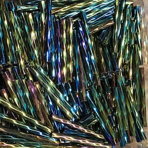 May include: A pile of iridescent glass rods in shades of blue, green, and gold. The rods are twisted and have a reflective surface.