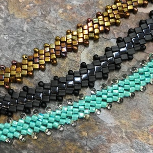May include: Three beaded bracelets in different colors and patterns. The top bracelet is gold, the middle bracelet is black, and the bottom bracelet is turquoise.