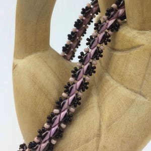 Op de afbeelding: Een kralenarmband met afwisselende zwarte en roze kralen. De armband is gemaakt met kleine, ronde kralen en heeft een delicate, vrouwelijke uitstraling.