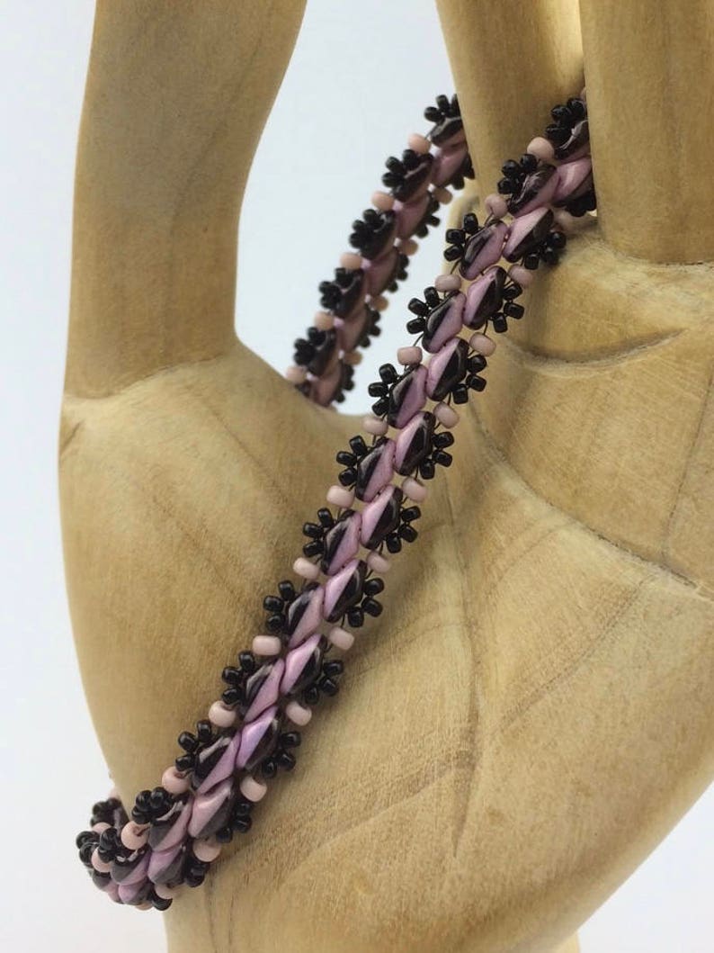 Op de afbeelding: Een kralenarmband met afwisselende zwarte en roze kralen. De armband is gemaakt met kleine, ronde kralen en heeft een delicate, vrouwelijke uitstraling.