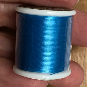 May include: A spool of bright blue thread in a clear plastic container with a white lid.